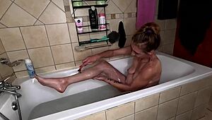 Skinny milf strips red dress, shaves legs and pussy in bubbly bath.